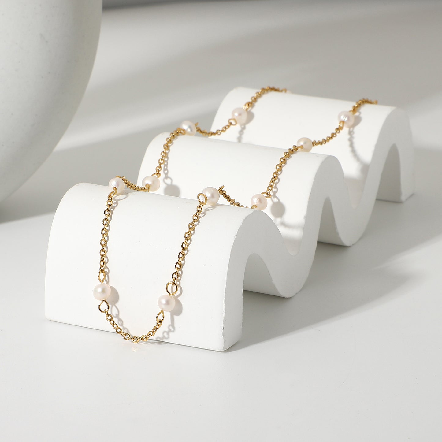 Gold chain necklace with pearls on a white wavy stand against a light background