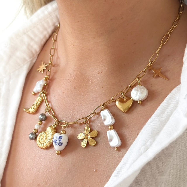 Necklace with various charms including pearls, flowers, and stars on a person wearing a white shirt.