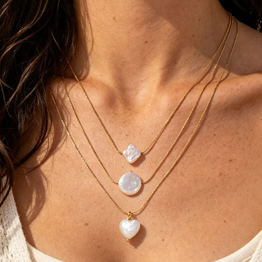 Close-up of a woman wearing gold necklaces with pearl pendants.