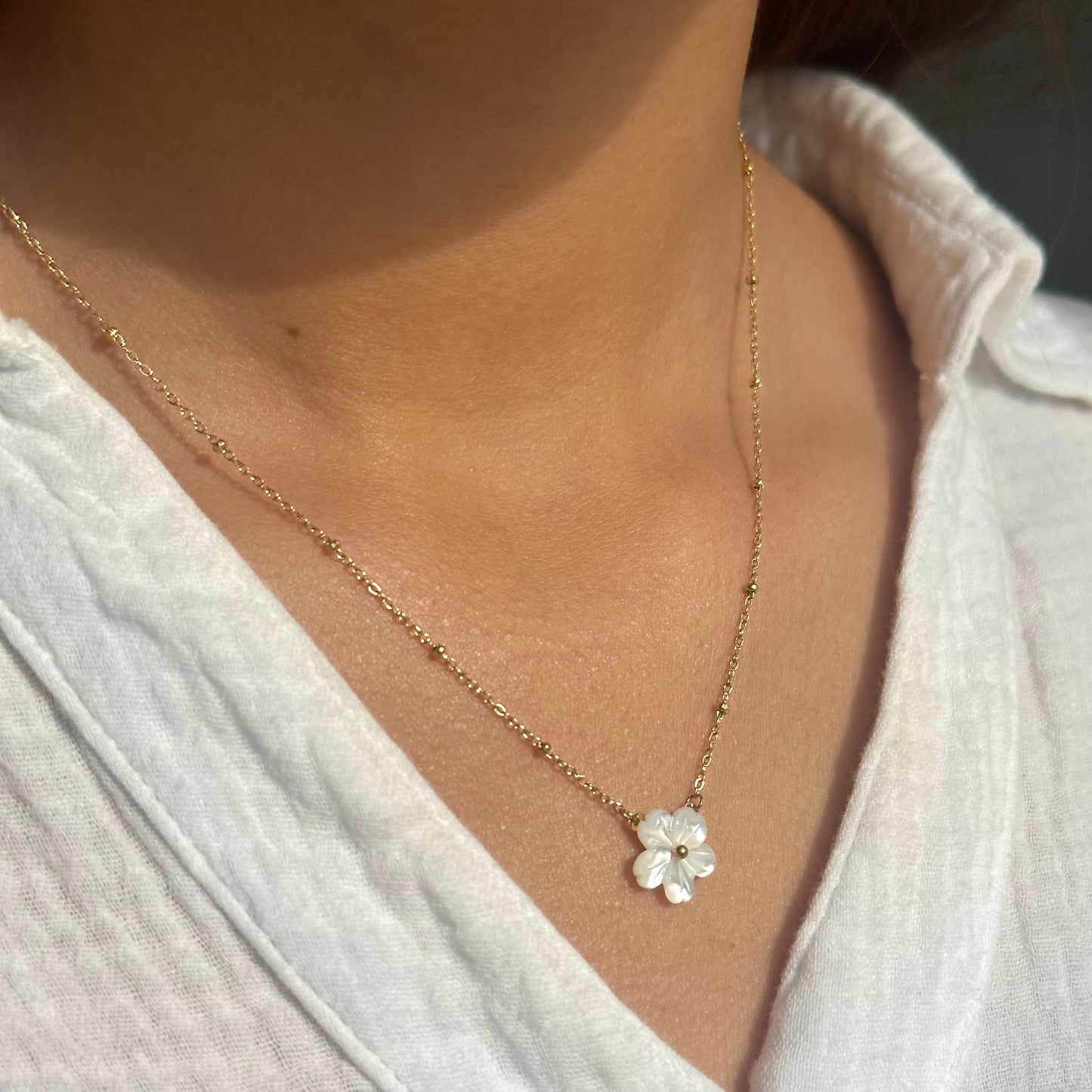 Necklace with a floral pendant worn by a person in a white shirt