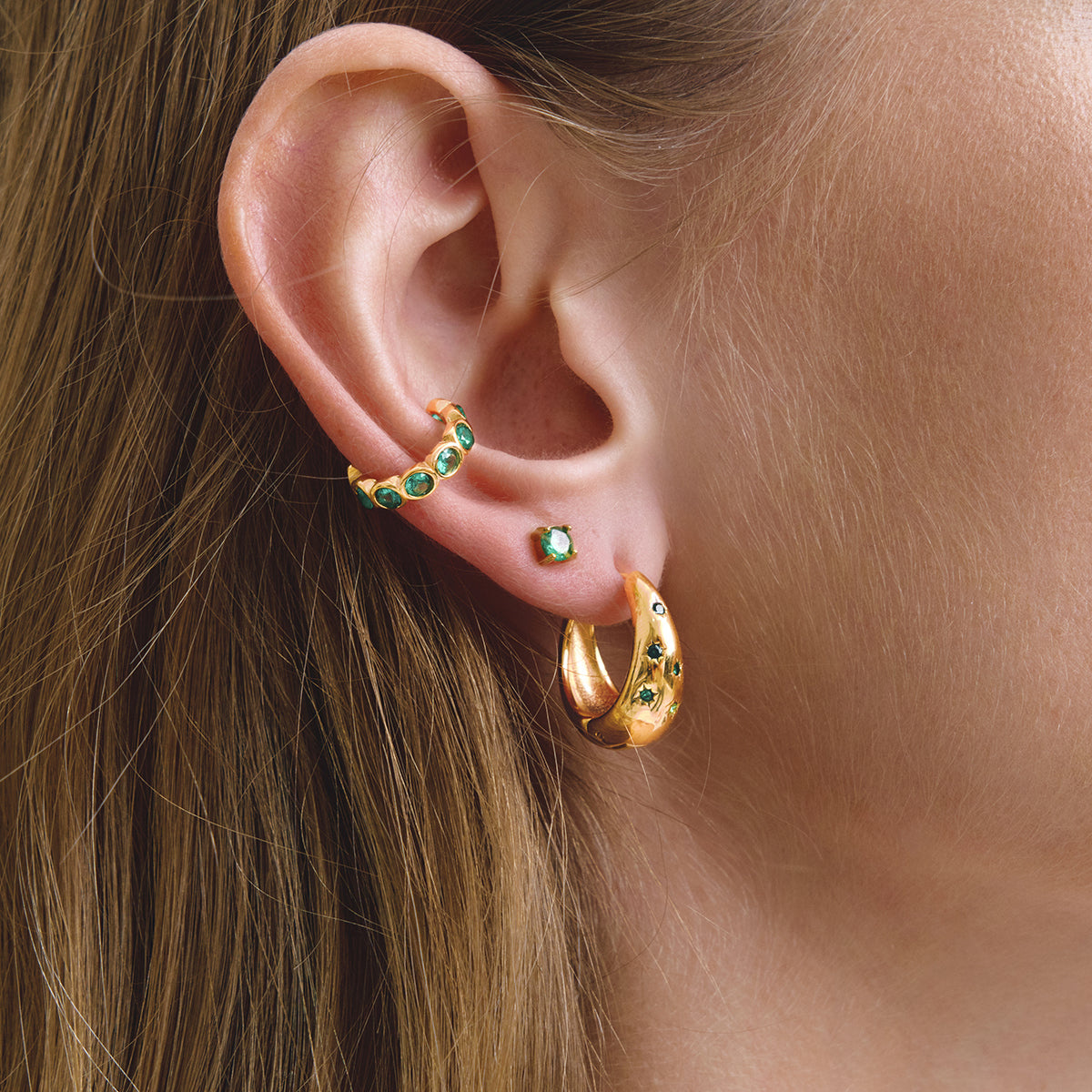 Gold hoop earrings with green gemstones worn by a person