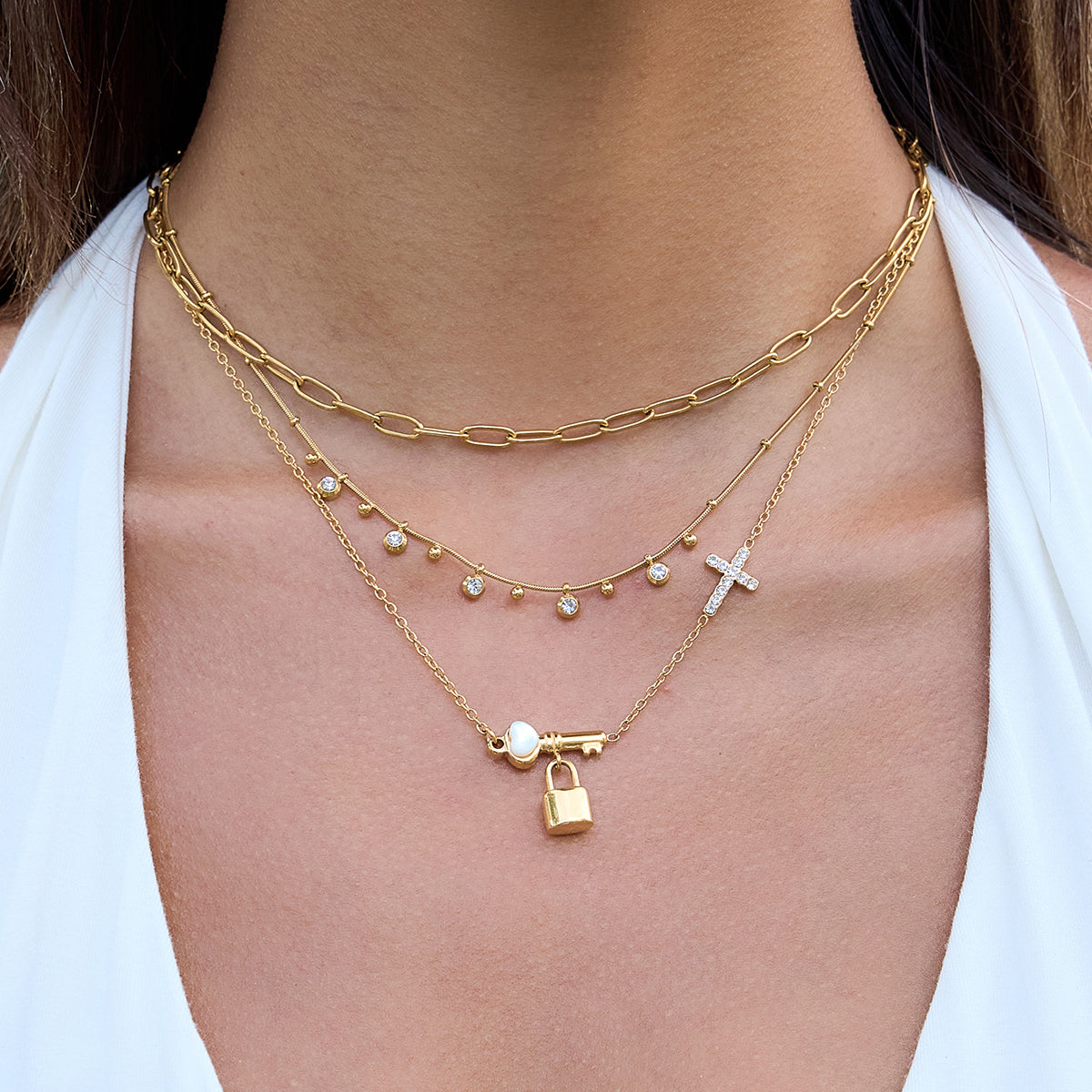 Gold necklaces with various charms on a person wearing a white top.