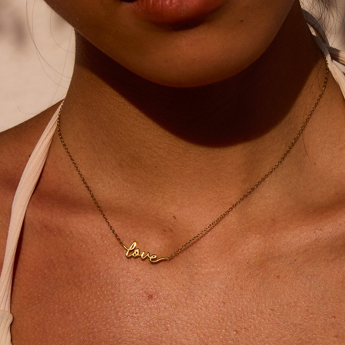 Gold 'love' necklace on a person's neck with a warm color tone.
