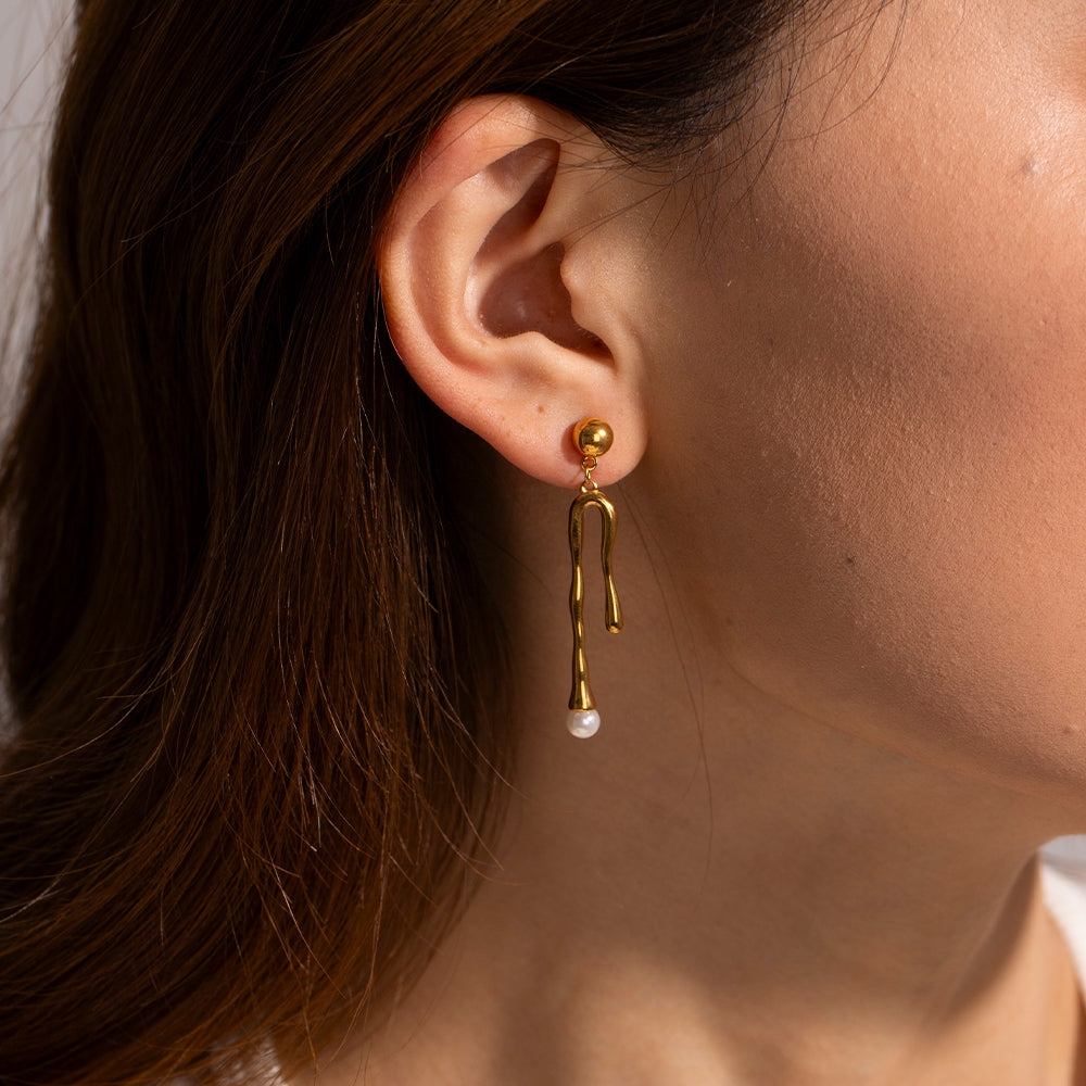 Asymmetrical Gold earring with a pearl drop worn by a person