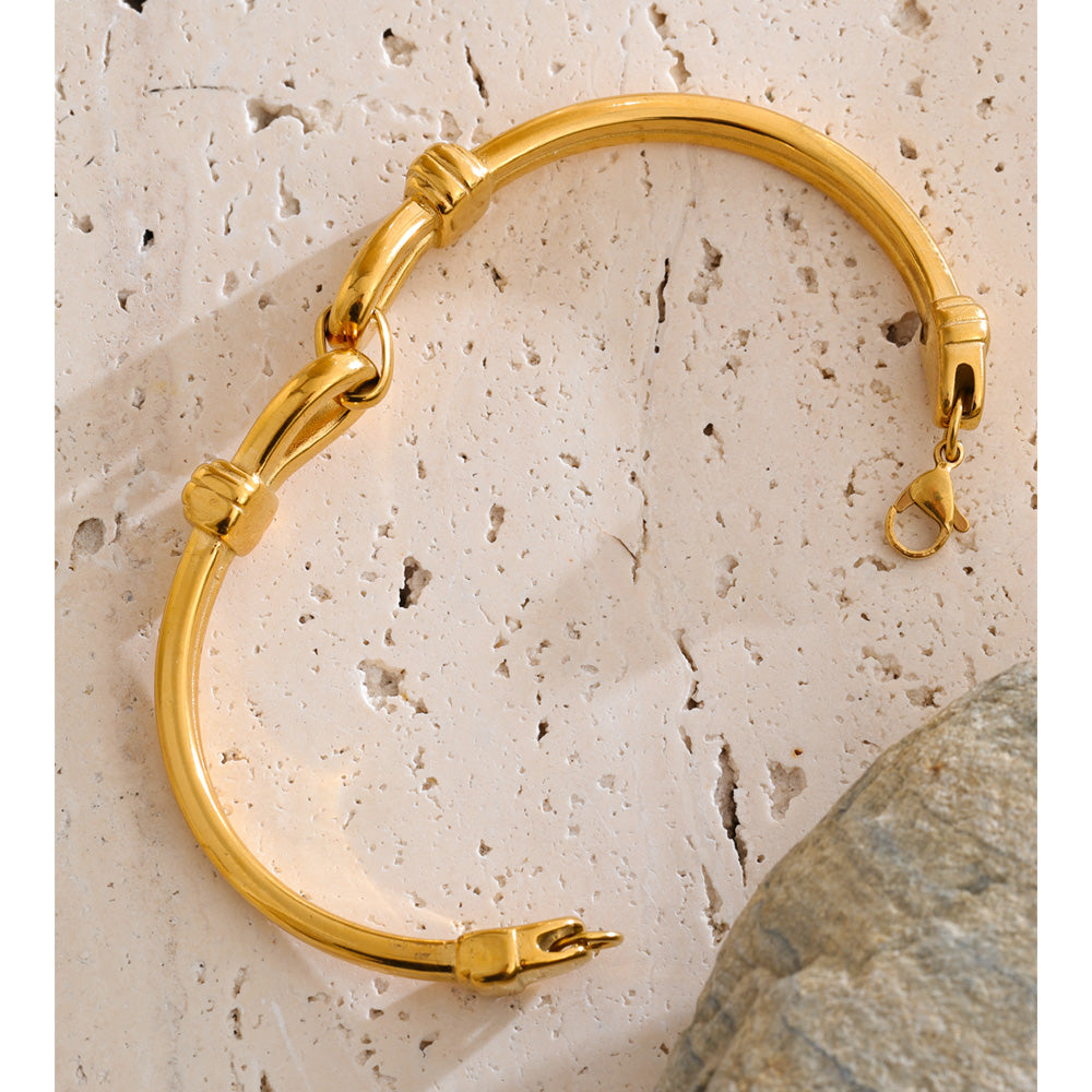 Gold bracelet on a textured beige surface with a stone in the background