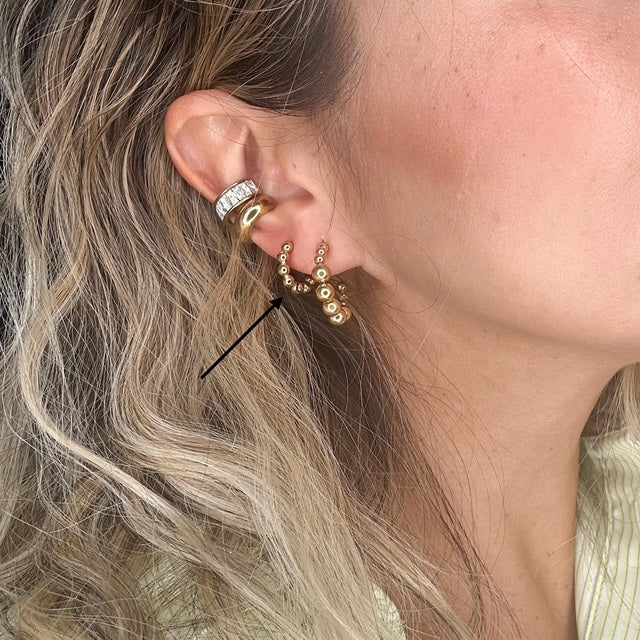 Close-up of an ear wearing gold hoop earrings with a blurred background