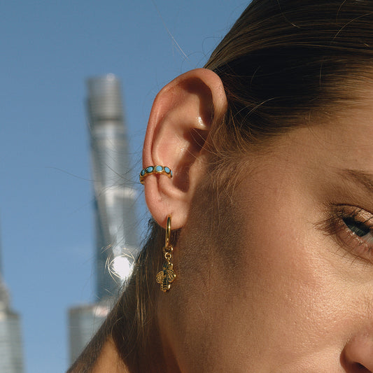 Close-up of a person's ear with earrings against a city skyline.