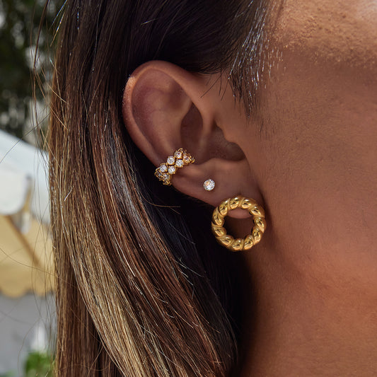 Close-up of an ear wearing gold hoop earrings with a blurred outdoor background