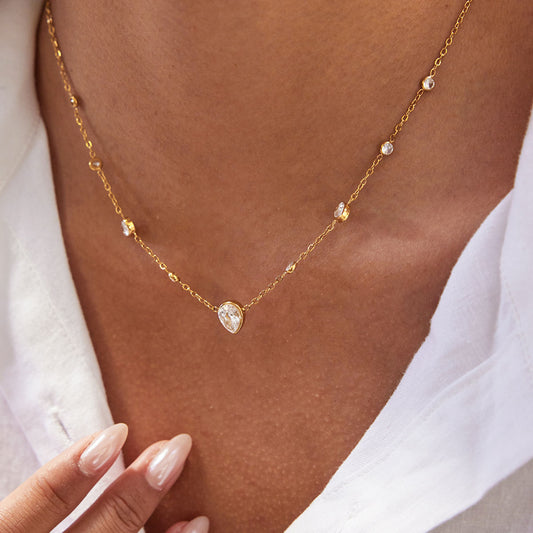 Gold necklace with a central gemstone worn by a person, against a neutral background.