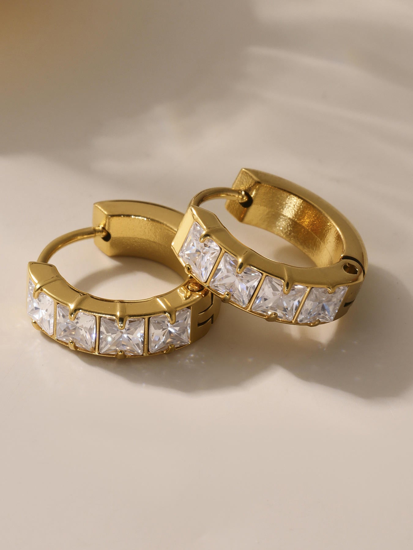 Gold hoop earrings with clear gemstones on a beige background