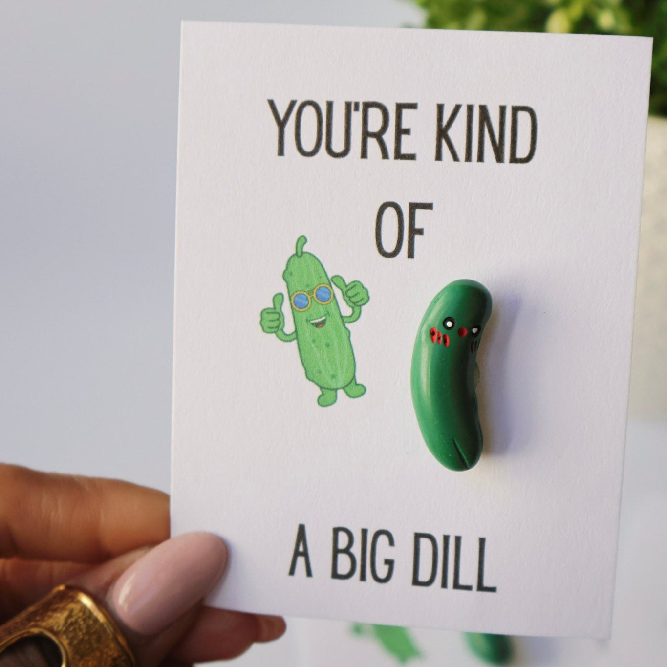 Card with a green dill pickle charm and text 'You're kind of a big dill' held by a hand.