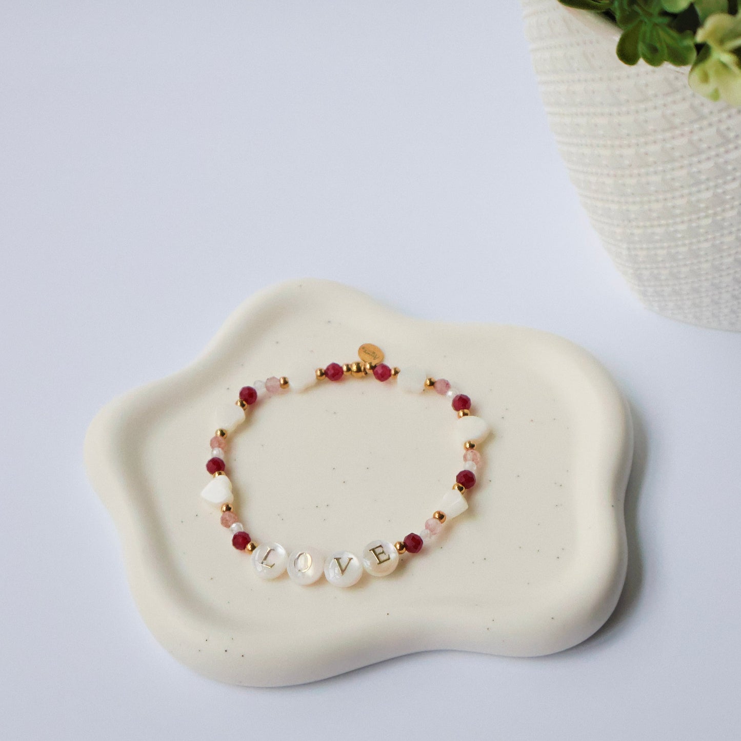 Bracelet with the word Love, red and white beads on a white stone surface with a plant in the background