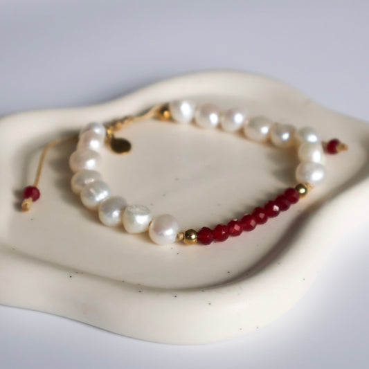 Pearl and red bead bracelet on a white dish with a gray background