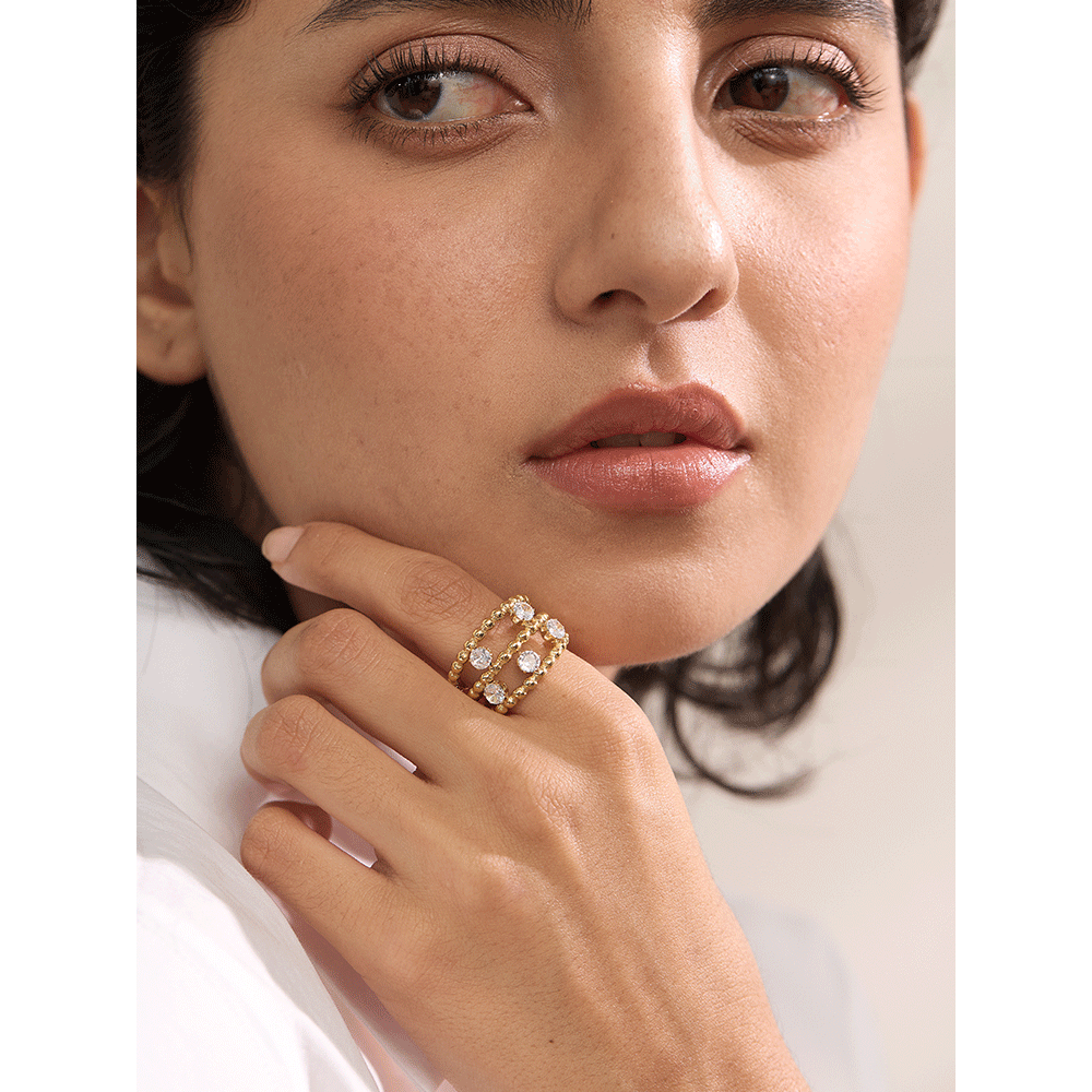 Close-up of a woman's hand wearing a gold ring with gemstones on a neutral background