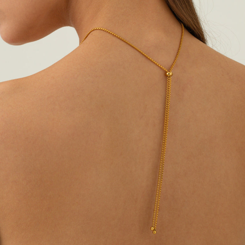 Woman wearing a gold back chain necklace against a neutral background