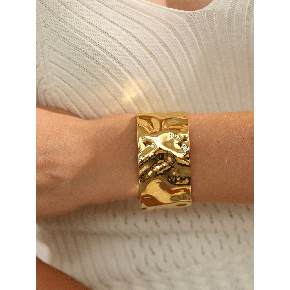 Gold bracelet on a wrist with a neutral background