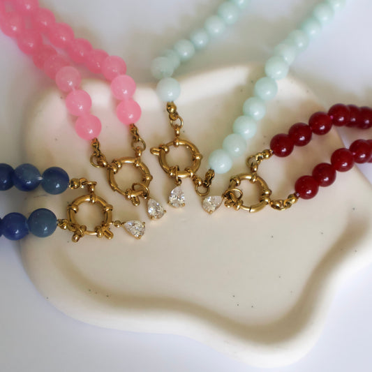 Four beaded necklaces in pink, blue, green, and red on a white surface.