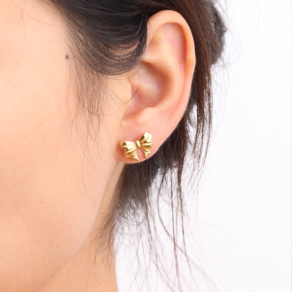 Gold bow-shaped earrings worn by a person with dark hair.