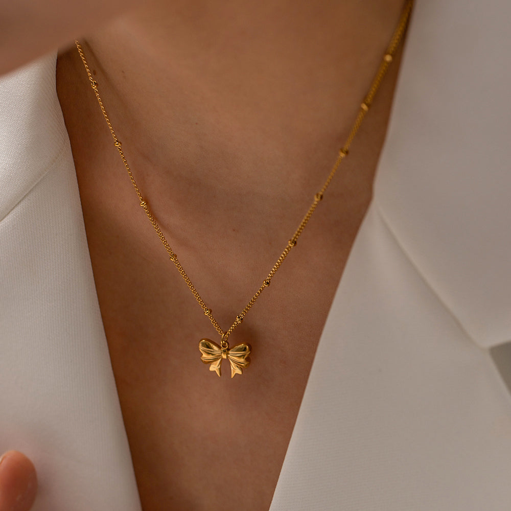 Gold necklace with a bow pendant on a person's neck against a neutral background