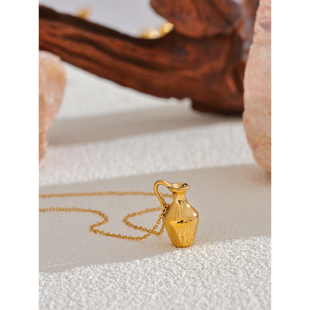 Gold alabaster vase pendant necklace on a textured surface with a blurred background