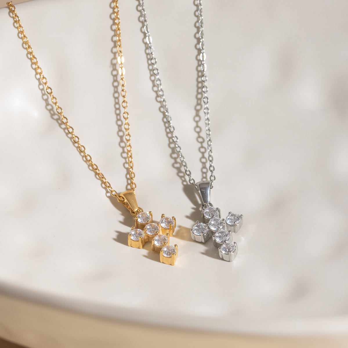 Two necklaces, one gold and one silver, with diamond pendants on a light background.