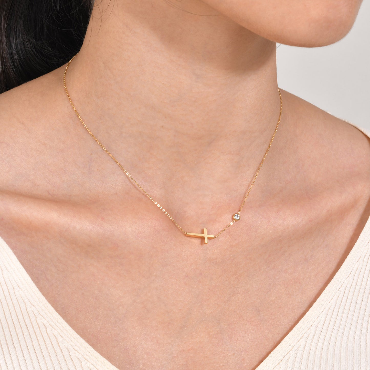 Gold necklace with a cross pendant on a person wearing a white top.