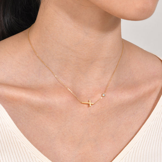 Gold necklace with a cross pendant on a person wearing a white top.