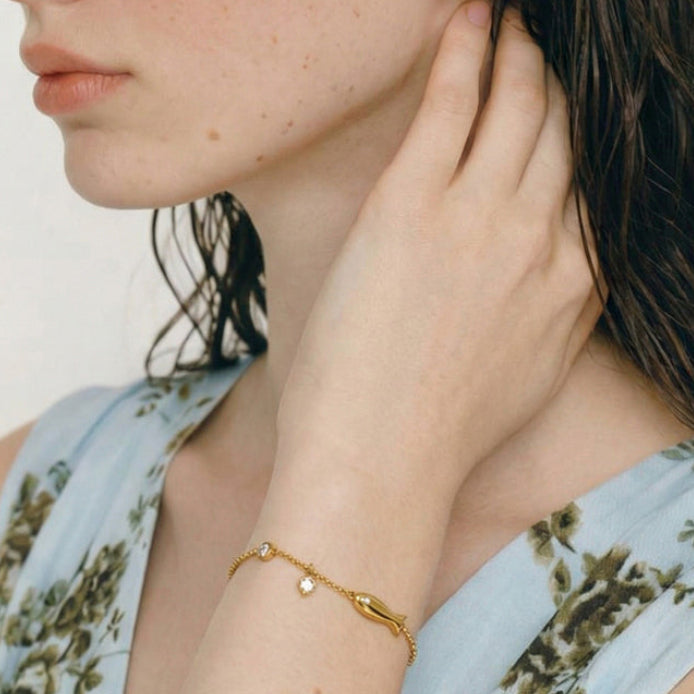 Follow Me gold-plated fish charm bracelet worn on a model’s wrist, showing the delicate chain and dangling crystal accent.