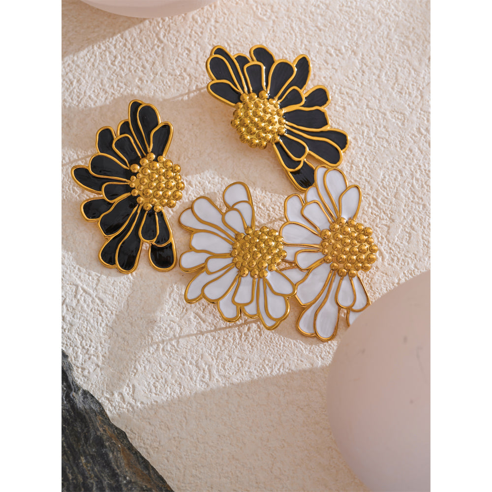 Floral earrings with black, gold, and white colors on a textured surface.
