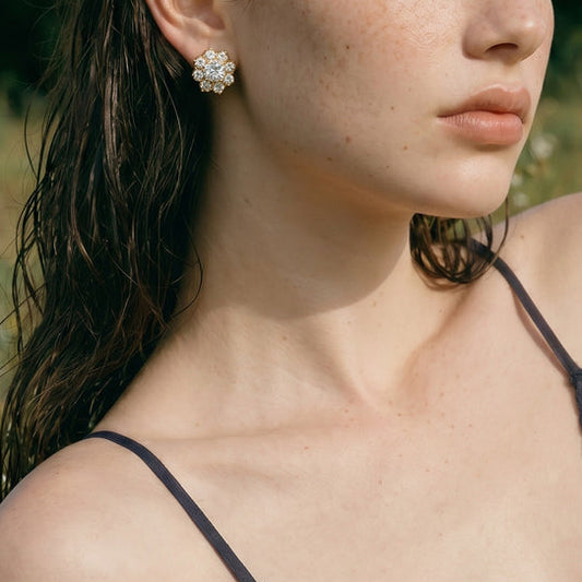 Model wearing Bloom 18K gold-plated flower stud earrings with sparkling clear zircon stones, styled with a green plaid dress outdoors.