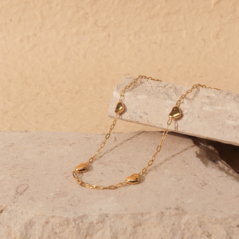 Gold choker with heart-shaped charms on a beige stone surface