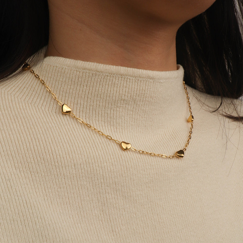 Gold heart-shaped necklace on a person wearing a beige sweater