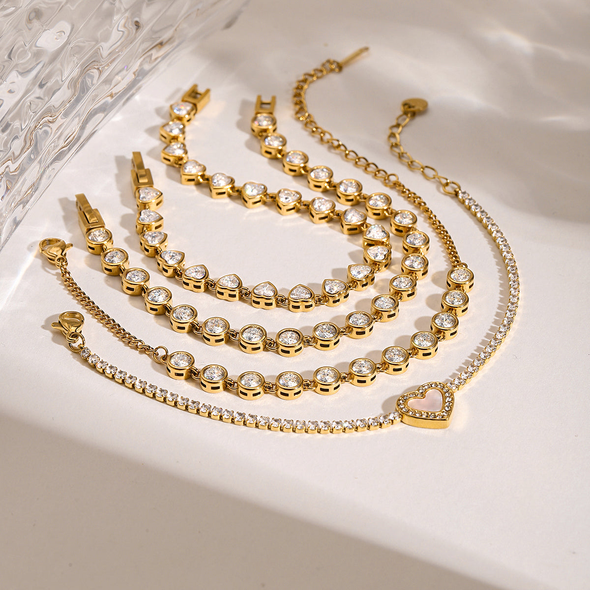 Gold bracelets with heart-shaped clasps on a white surface