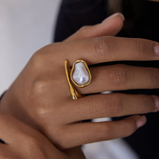 Gold ring with a pearl-like stone on a hand against a neutral background