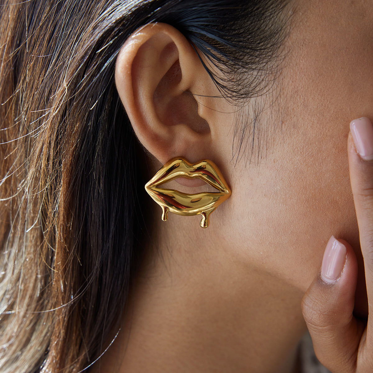 Gold lip-shaped earring worn by a person with dark hair.