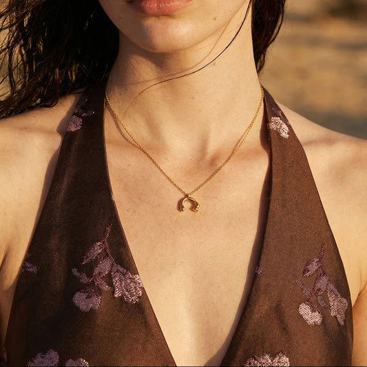 Elisa gold-plated necklace worn with a brown floral halter top, showing the curved pendant resting below the collarbone