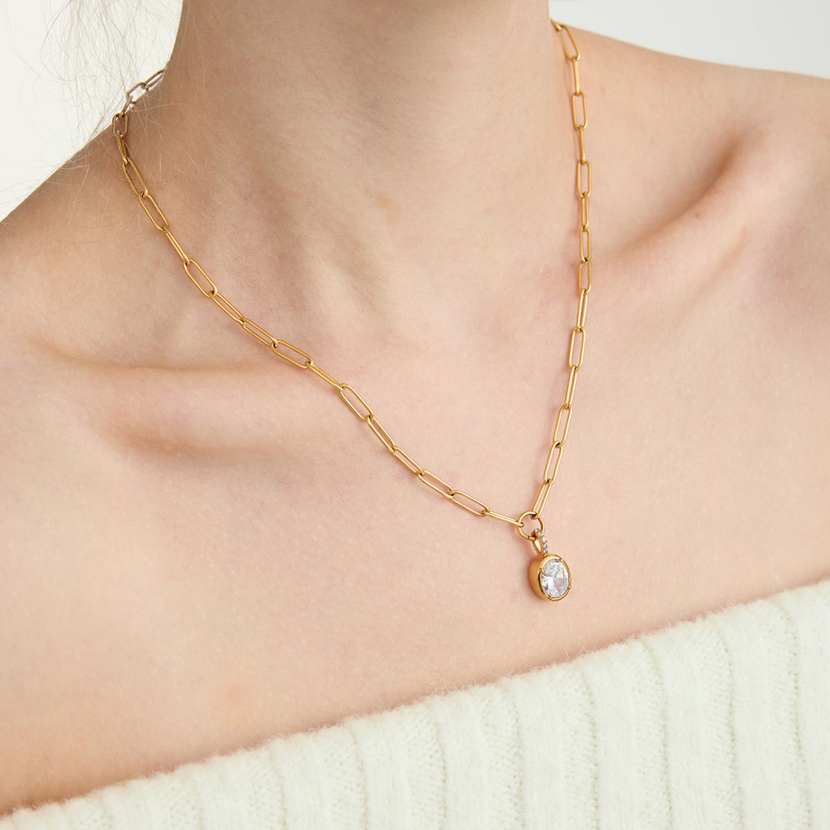 Gold chain necklace with a pendant on a person wearing a white sweater.