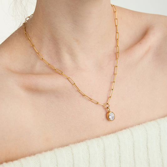 Gold chain necklace with a pendant on a person wearing a white sweater.