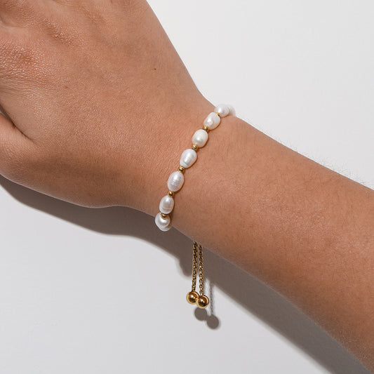 Pearl bracelet on a wrist with a gold charm against a white background