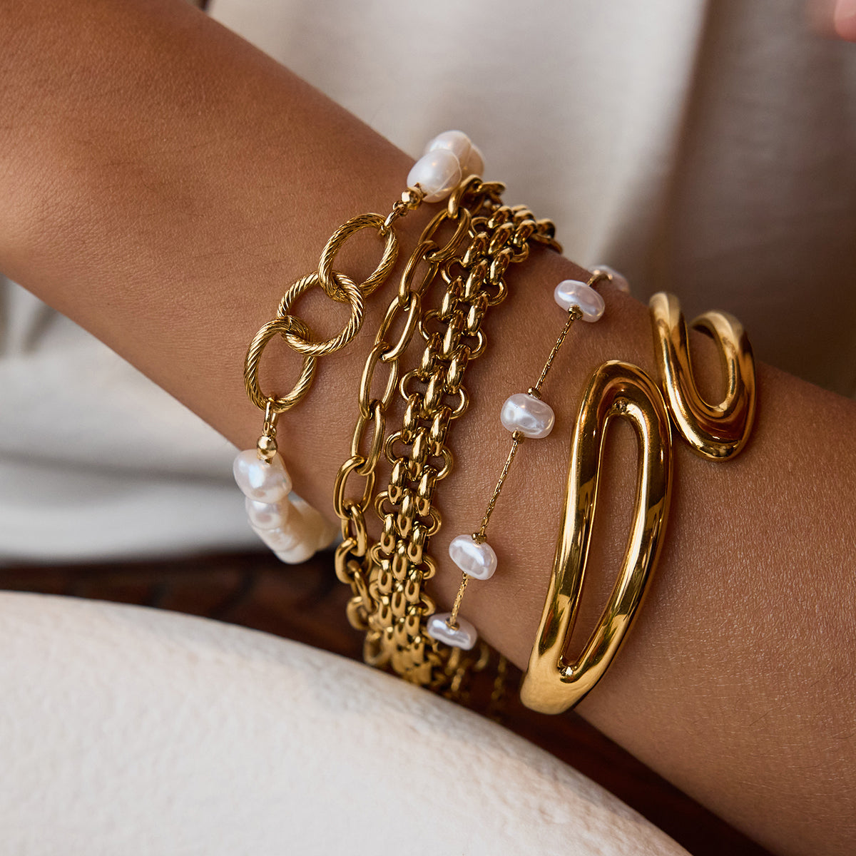 Gold bracelets with pearls on a wrist against a neutral background