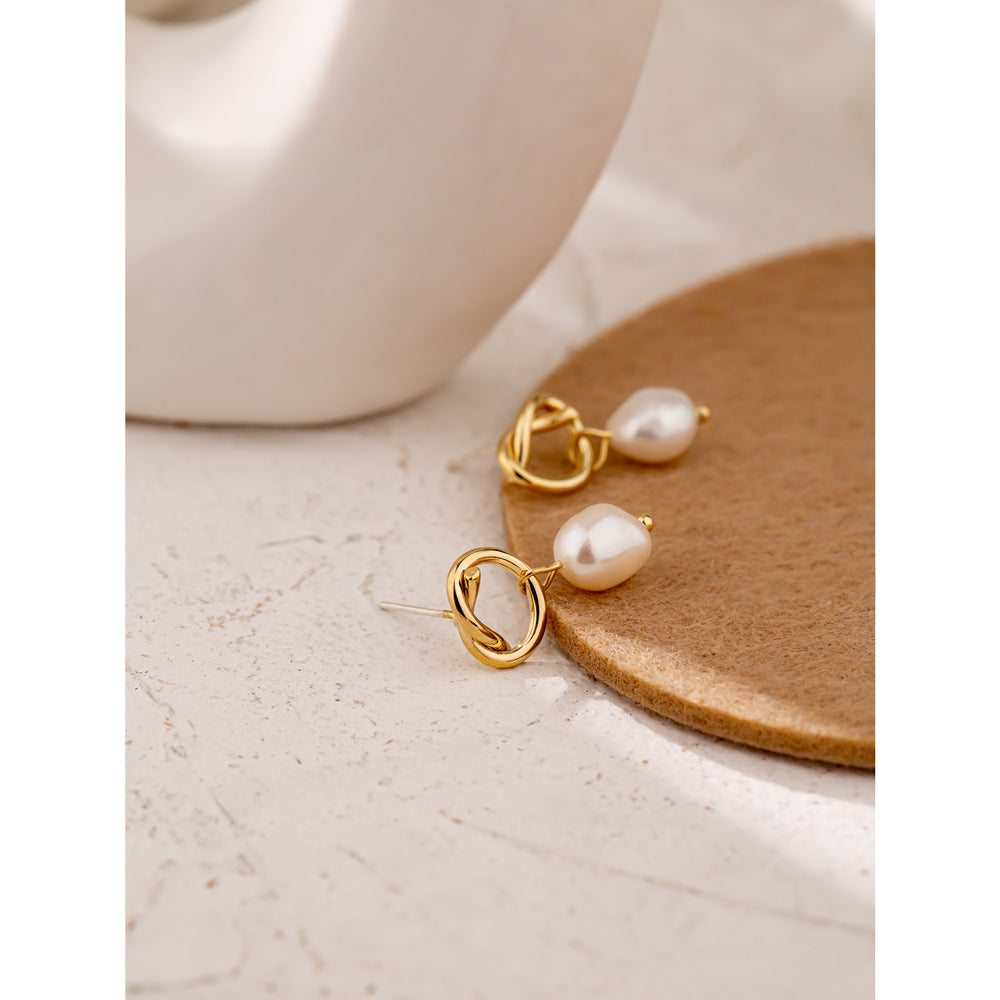 Gold earrings with pearls on a wooden coaster next to a white mug.