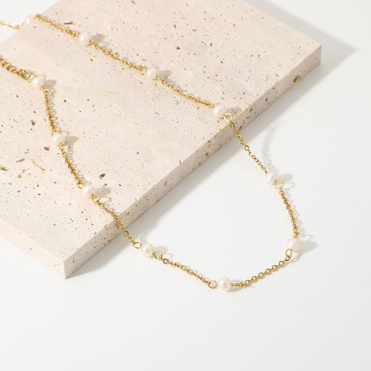 Gold necklace with pearls on a light stone surface