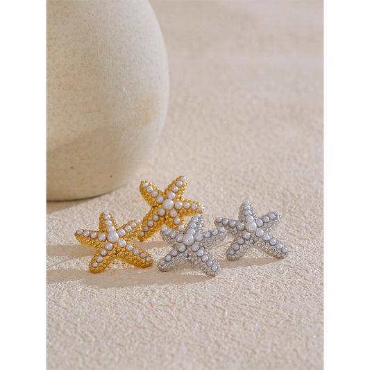 Star-shaped earrings in gold, silver, and pearl on a textured beige surface.