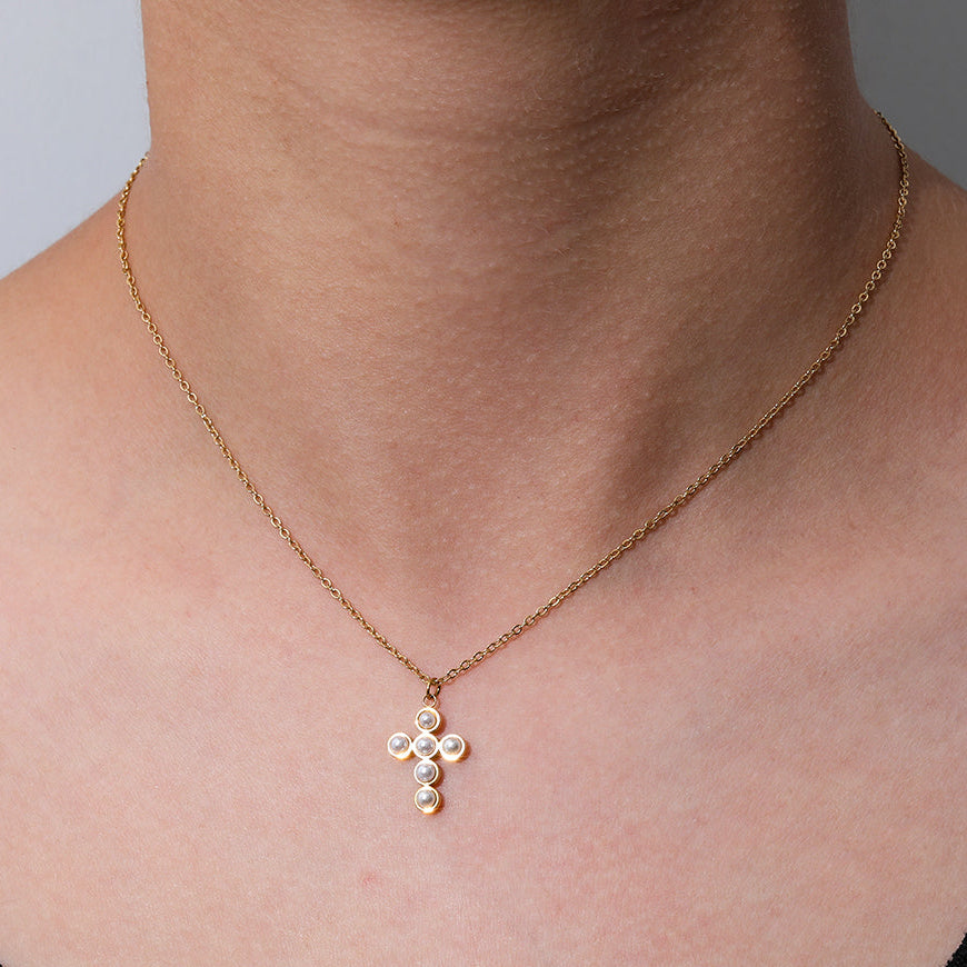 Gold necklace with a cross pendant on a person's neck against a neutral background