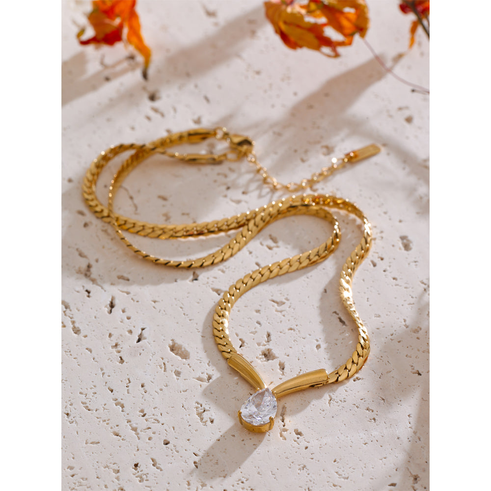 Gold necklace with a diamond pendant on a textured surface with flowers in the background