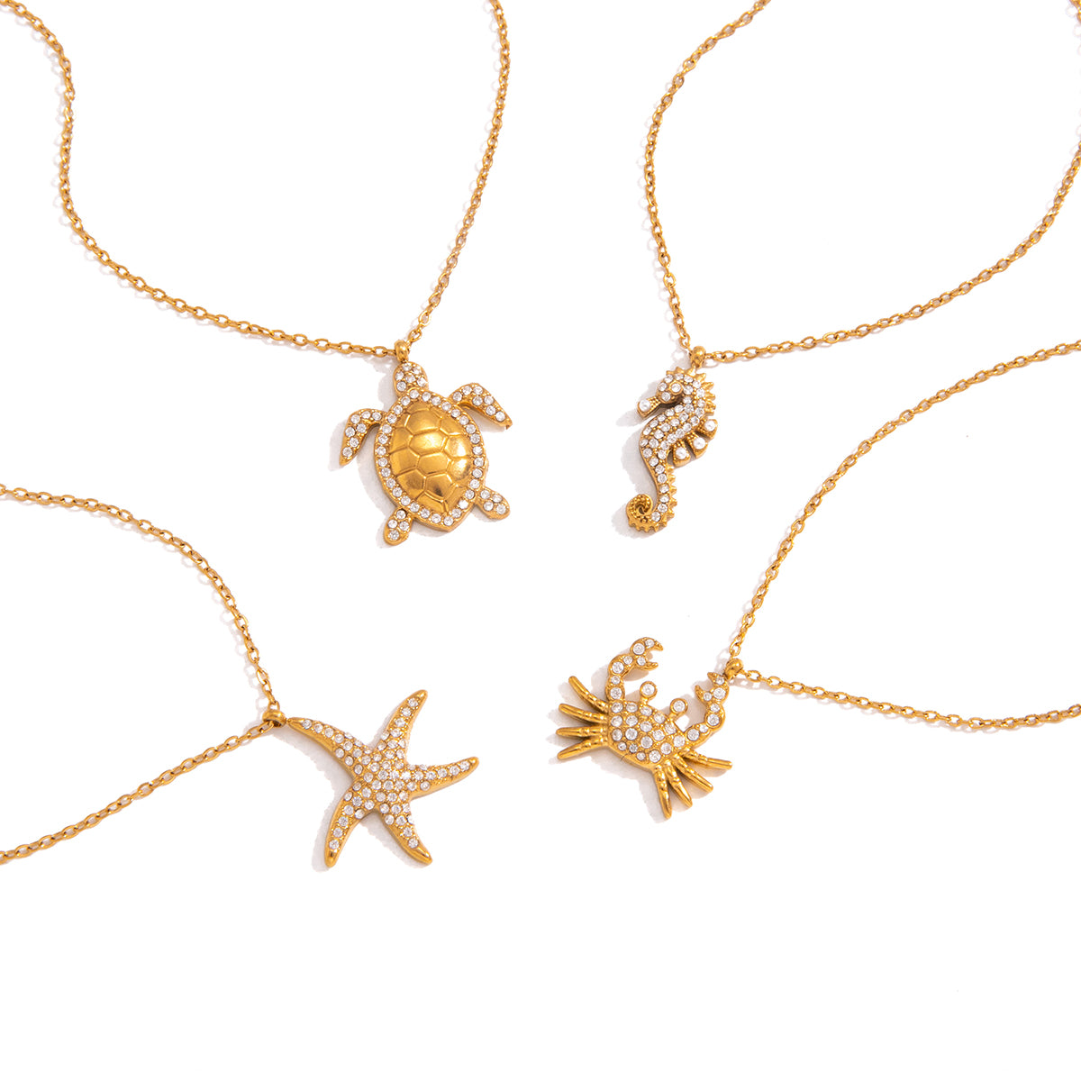 Four gold-tone ocean-themed necklaces with sea creature pendants, including a turtle, seahorse, starfish, and crab, decorated with small clear rhinestones, arranged on a white background.