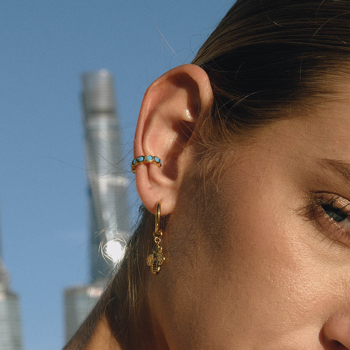 Close-up of a person's ear with earrings against a city skyline.