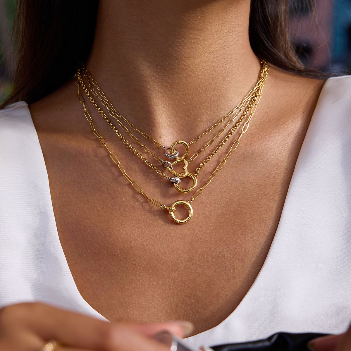 Close-up of a person wearing multiple gold necklaces on a blurred background