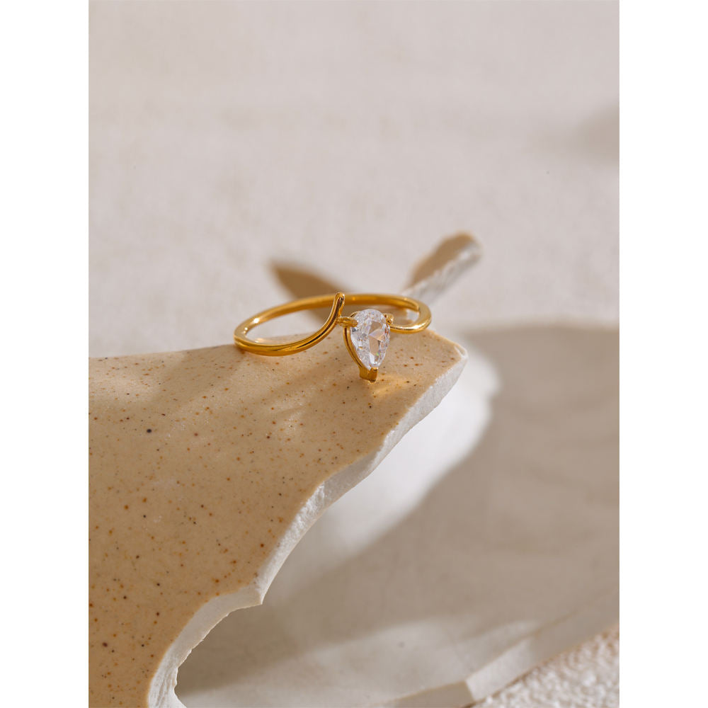 Gold ring with a clear gemstone on a textured beige surface