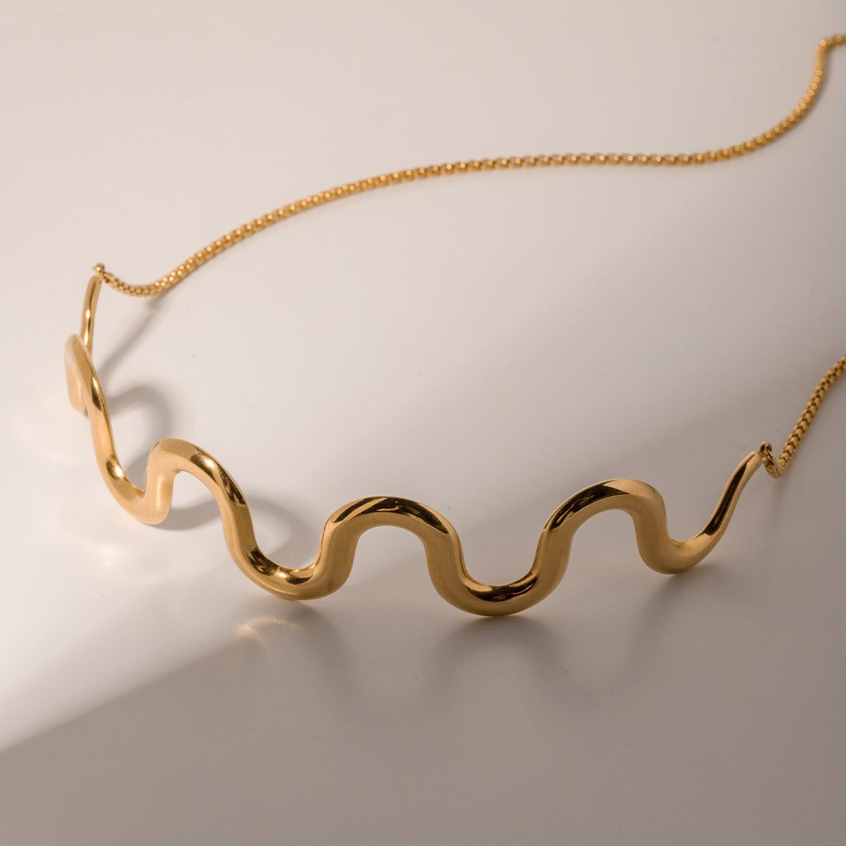Gold wavy necklace on a beige background